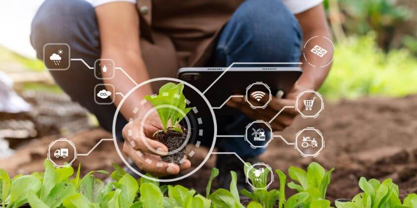 Farmer kneels down to plant a crop. there is a computer-like overlay with various icons in the photo.