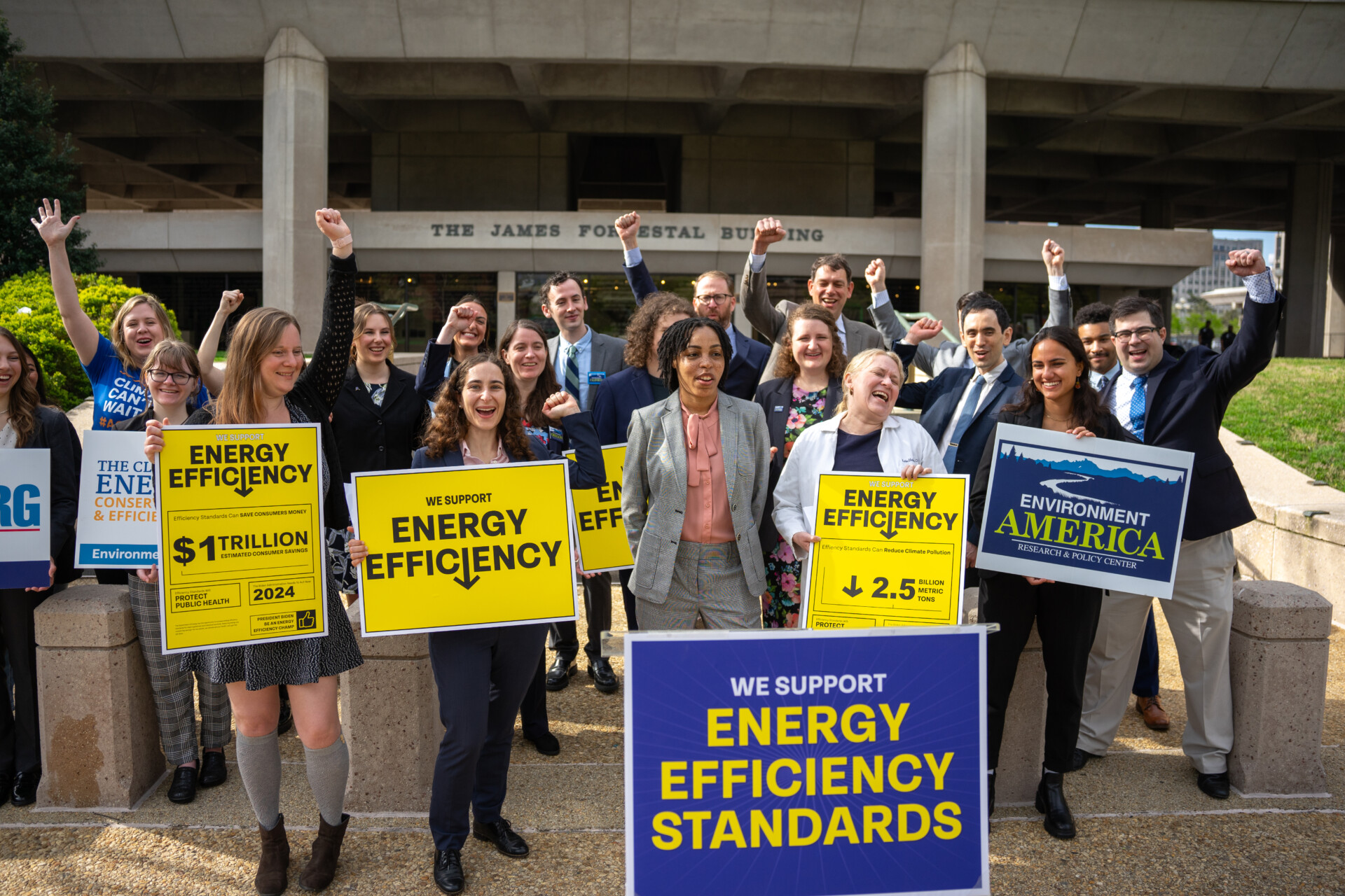 Image of people standing in a small crowd, in various stages of celebration and holding signs.